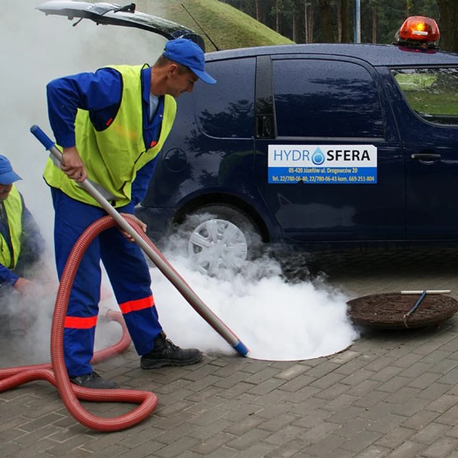 Pracownicy Hydrosfery czyszczą studzienkę kanalizacyjną przy samochodzie spółki